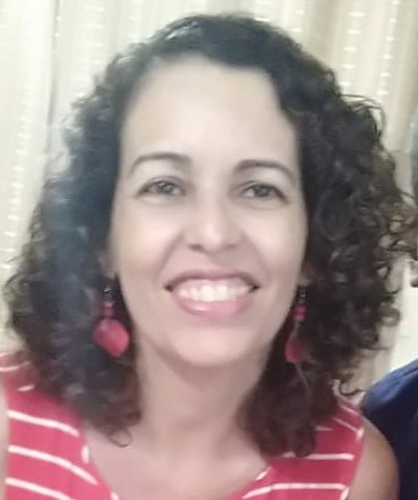 Foto da professora Luciana, uma mulher sorridente de cabelos encaracolados, brincos vermelhas e uma blusa vermelha com listras brancas horizontais