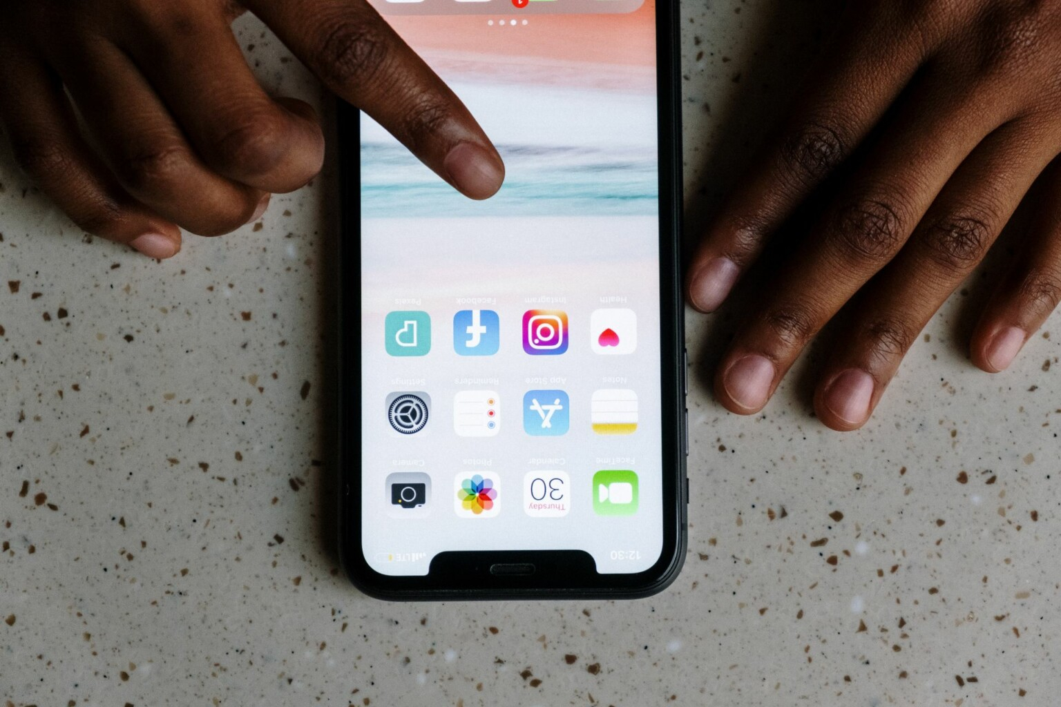 Imagem de um smartphone ligado e sendo tocado pelo dedo indicador de uma mão humana