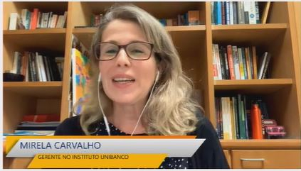 Imagem de uma mulher loira de cabelos lisos e óculos de grau. Ela está de fones de ouvido e falando. A imagem é de um print da tela enquanto ela estava em uma videochamada