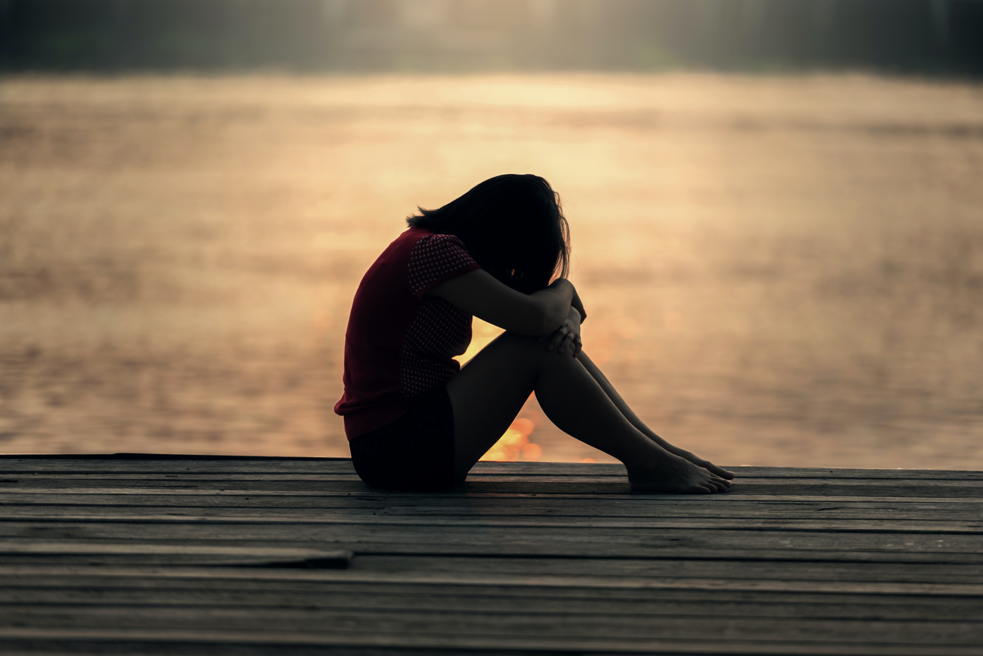 Uma menina triste sentada em um deque de madeira com um lago ao fundo