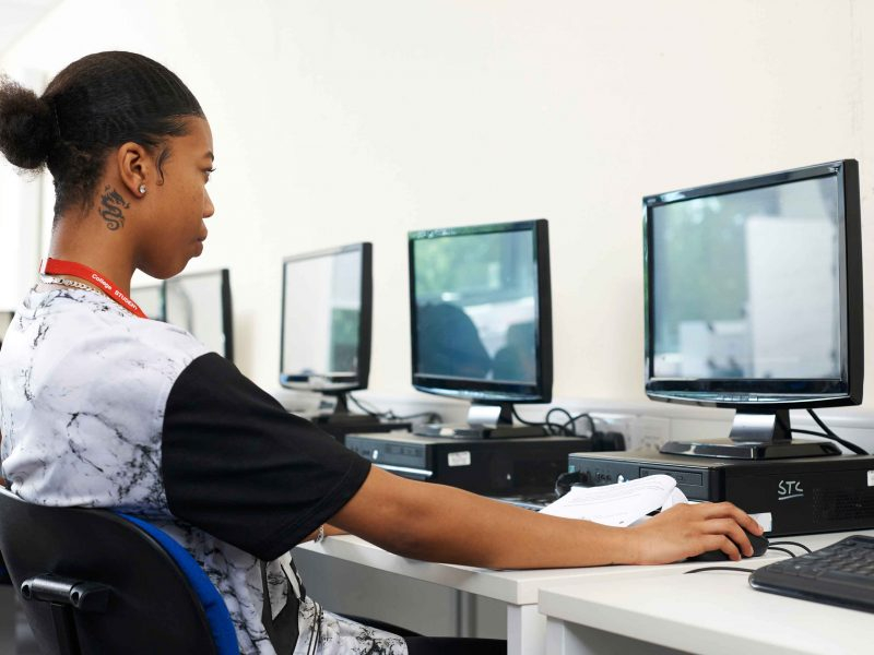 Adolescente negra esta sentada em uma cadeira e usando um computador à sua frente, mexendo no mouse
