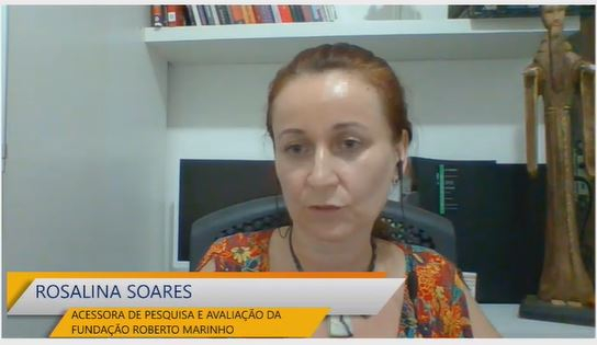 Print de uma tela mostrando videochamada. Aparece uma mulher de cabelos claros e presos falando. Ela está de fones de ouvido