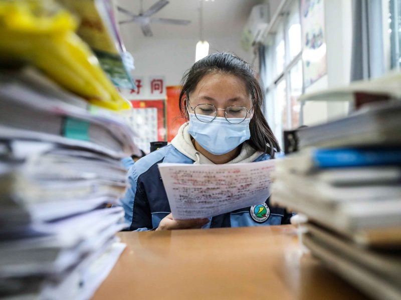 Imagem de uma jovem menina asiática de óculos e máscara de prevenção à covid-19 lendo um livro
