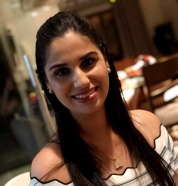 Mulher branca, de cabelos pretos e longos está sorrindo para quem fez a foto
