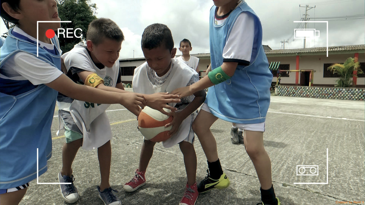 Quatro crianças em uma quadra poliesportiva disputando a posse de uma bola de basquete