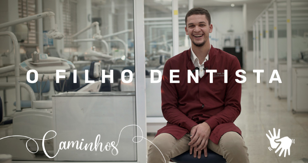 Um jovem rapaz branco está sentado em uma cadeira e está bem sorridente para quem bateu a foto. Há uma arte na imagem com os dizeres "O filho dentista"