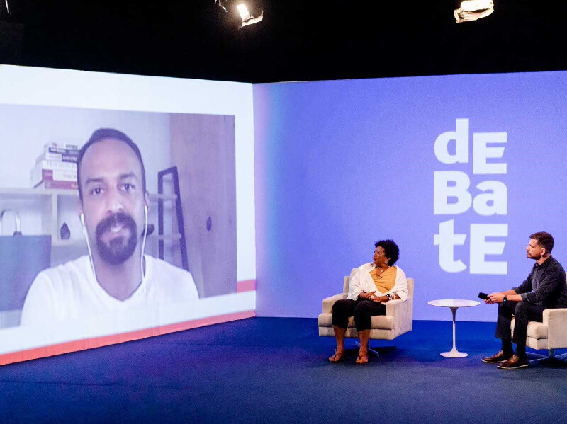 Imagem do jornalista correspondente na África do Sul no telão no cenário do programa Debate