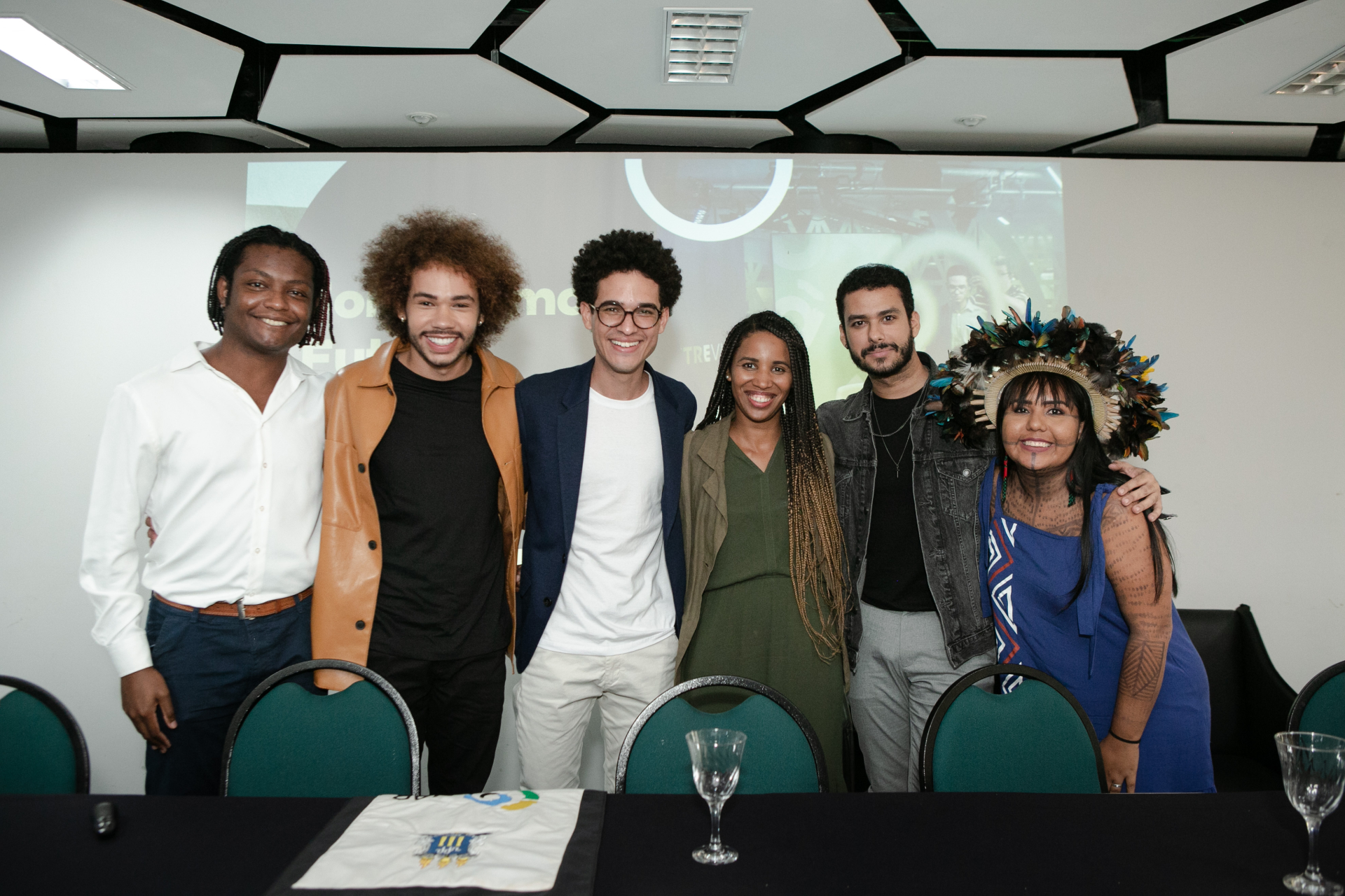 Seis pessoas estão de pé, sorrindo para a fotógrafa. Quatro homens e três mulheres.