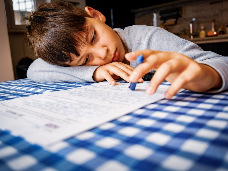 Um menino está estudando em casa bem desmotivado e cabisbaixo