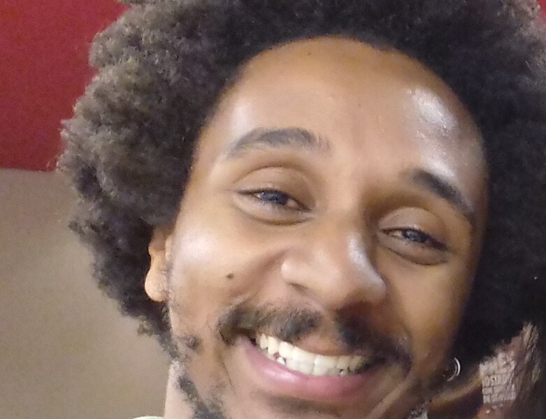 Rosto do professor Everton, que é um homem negro, de cabelo black power, nariz largo, bigode e ele está com um sorriso amplo