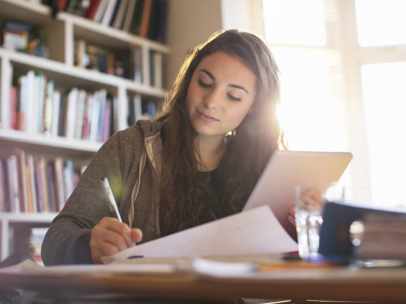 Uma adolescente está escrevendo algo em uma folha e segurando um livro