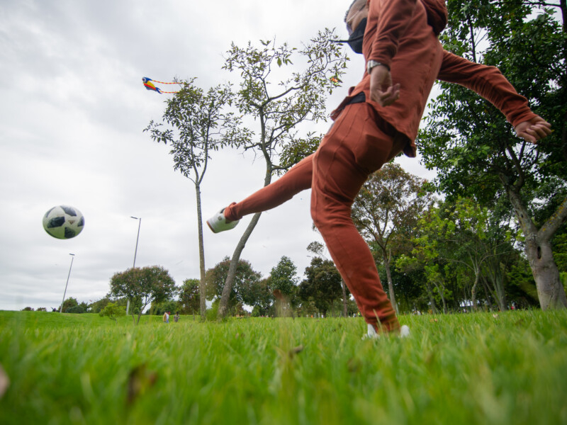 Um menino de máscara de prevenção à covid está chutando uma bola em um campo ao ar livre
