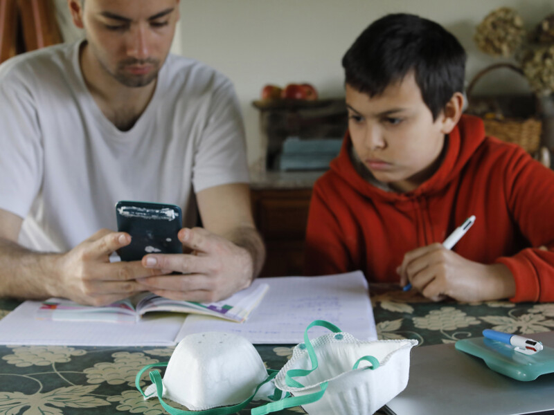 Um menino está estudando em casa ao lado de quem deve ser o seu pai