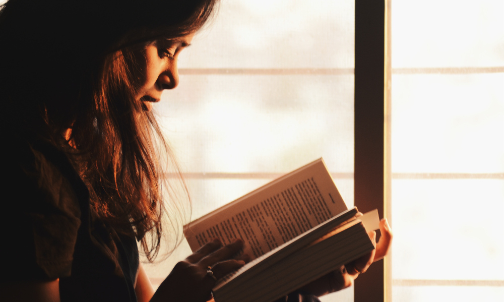 Uma menina, de perfil para quem bateu a foto, está lendo um livro