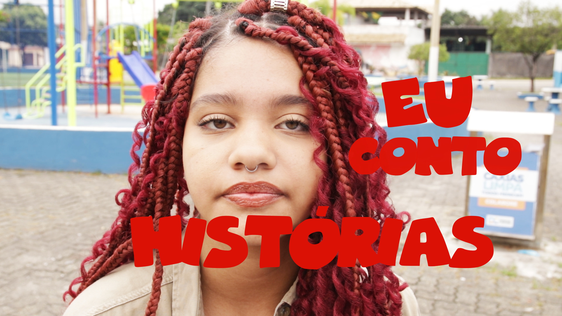 Uma jovem de cabelo trançado em tom avermelhado olha para quem a fotografa. Sobre sua imagem, a frase "Eu conto histórias", em vermelho.