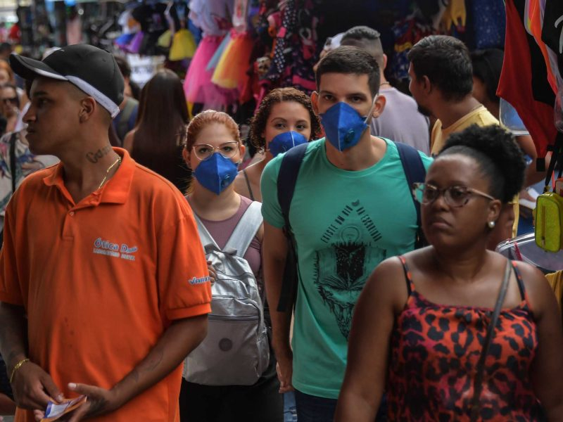 Imagem de pedestres andando pela rua. Alguns estão com máscaras de prevenção à covid e outros não