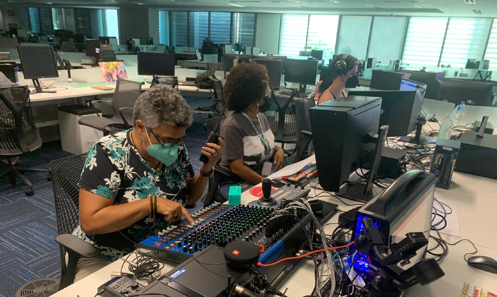 imagem de uma redação de TV, com várias baias e pessoas trabalhando sentadas diante de seus computadores
