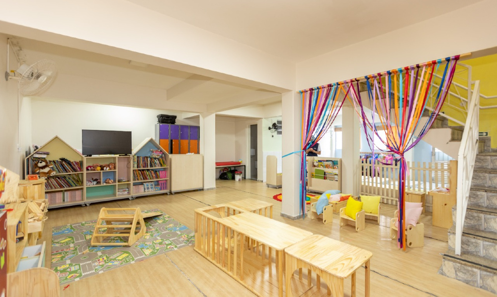 Um cômodo bem organizado, colorido e com espaço infantil, tendo uma mini biblioteca, cadeirinhas, etc