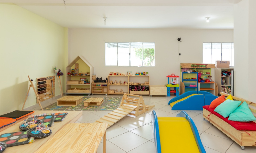 Um cômodo bem organizado, colorido e com espaço infantil, tendo uma mini biblioteca, cadeirinhas, etc