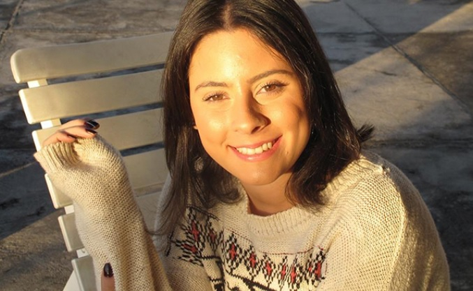 Mulher morena de cabelos lisos e de comprimento até os ombros está sorrindo para quem bateu a foto