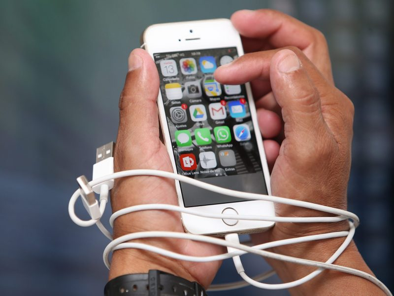 As duas mãos de uma pessoa estão enroladas no cabo de carregar a bateria de um celular e o celular está sendo segurado por estas mãos