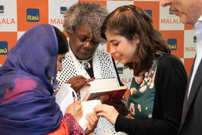 Uma mulher trajada com a vestimenta árabe está autografando um livro que será entregue à Tabata Amaral