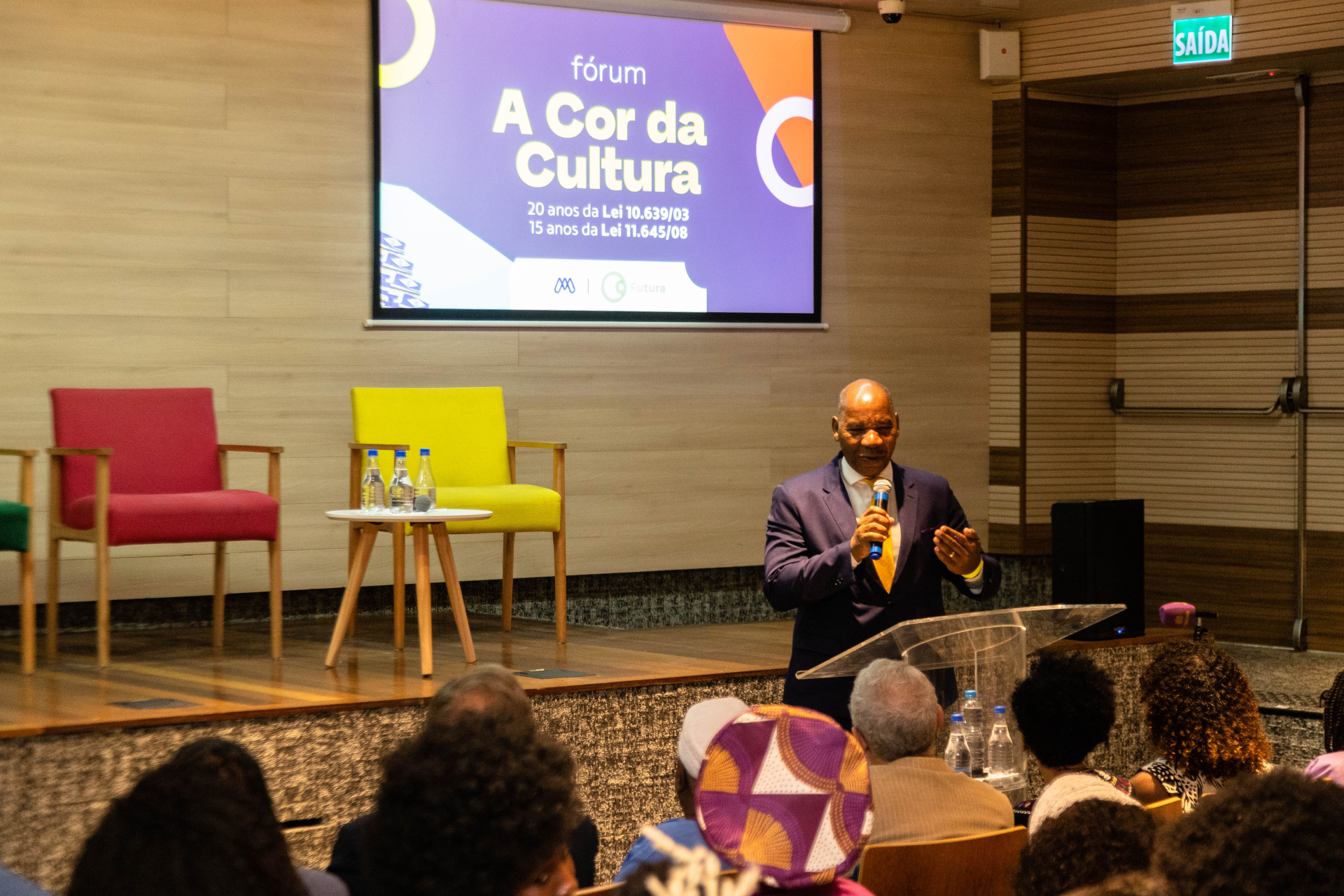 Um homem careca está de pé, diante de um púlpito e da plateia.