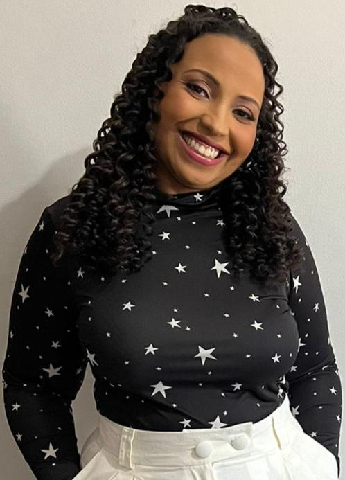Uma mulher sorri. Ela está com uma camisa preta, que tem estrelas brancas.