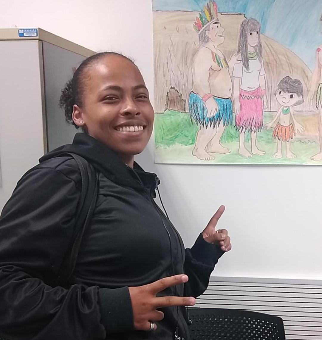 Mulher sorri e faz o gesto "paz e amor" com dedos indicador e médio em um formato de letra vê.