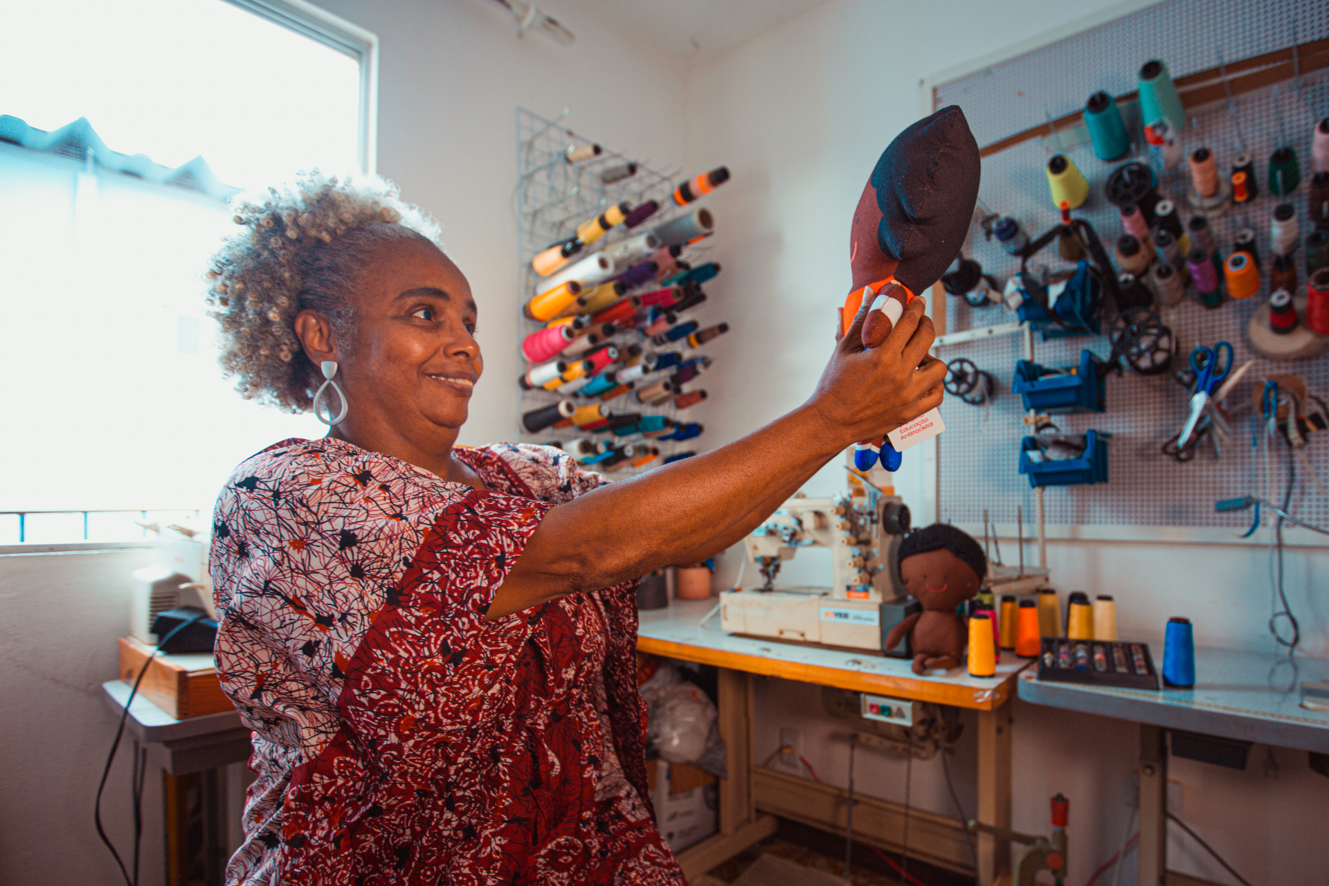 Uma senhora negra msorri enquanto olha para um objeto de artesanato que segura.