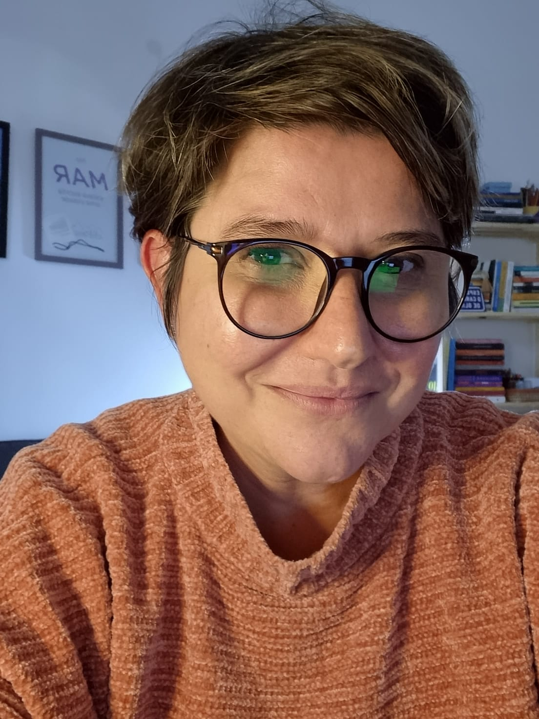 Mulher sorri. Ela usa óculos e tem cabelo curto.