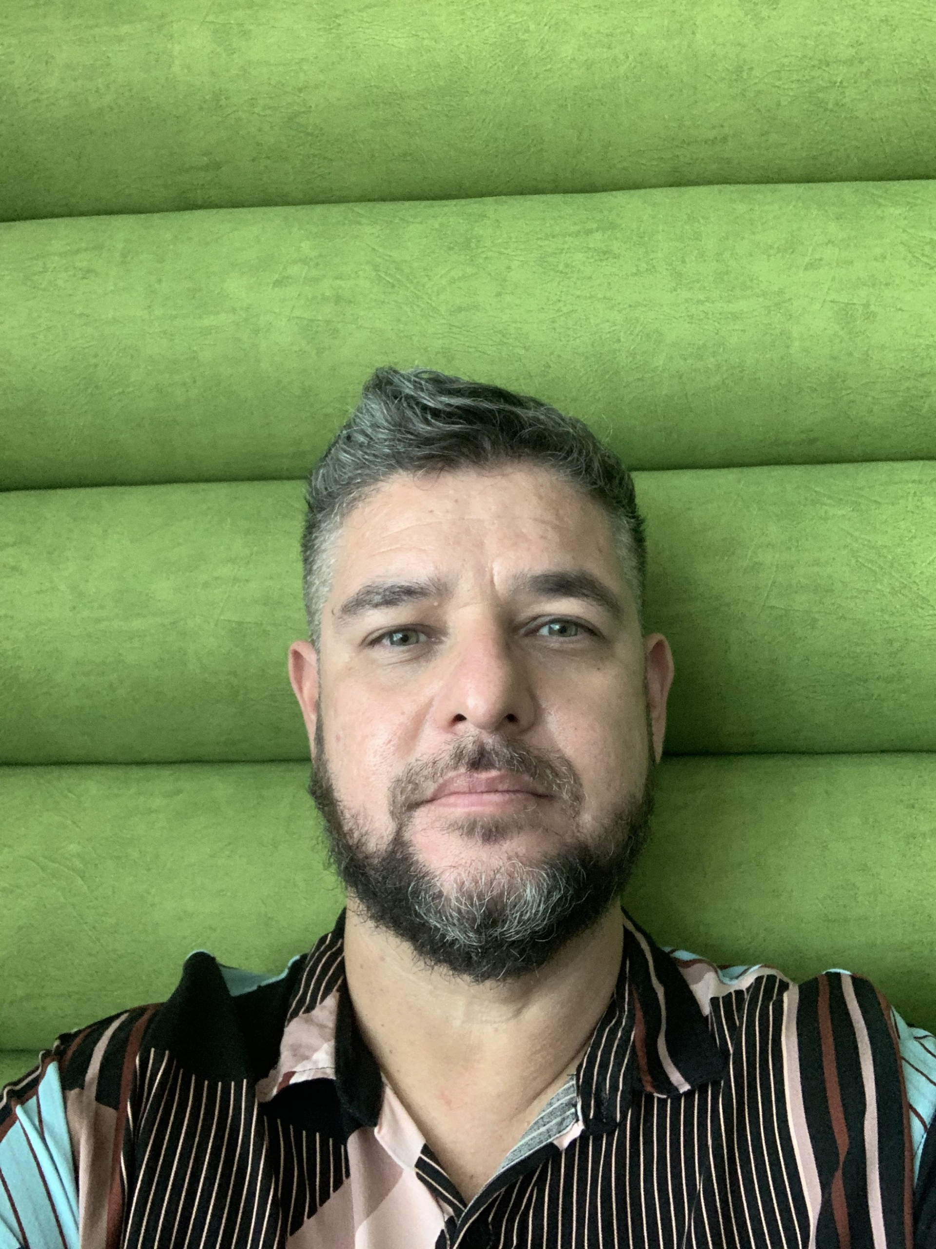 Homem dá leve sorriso. Atrás dele, um fundo acolchoado verde.