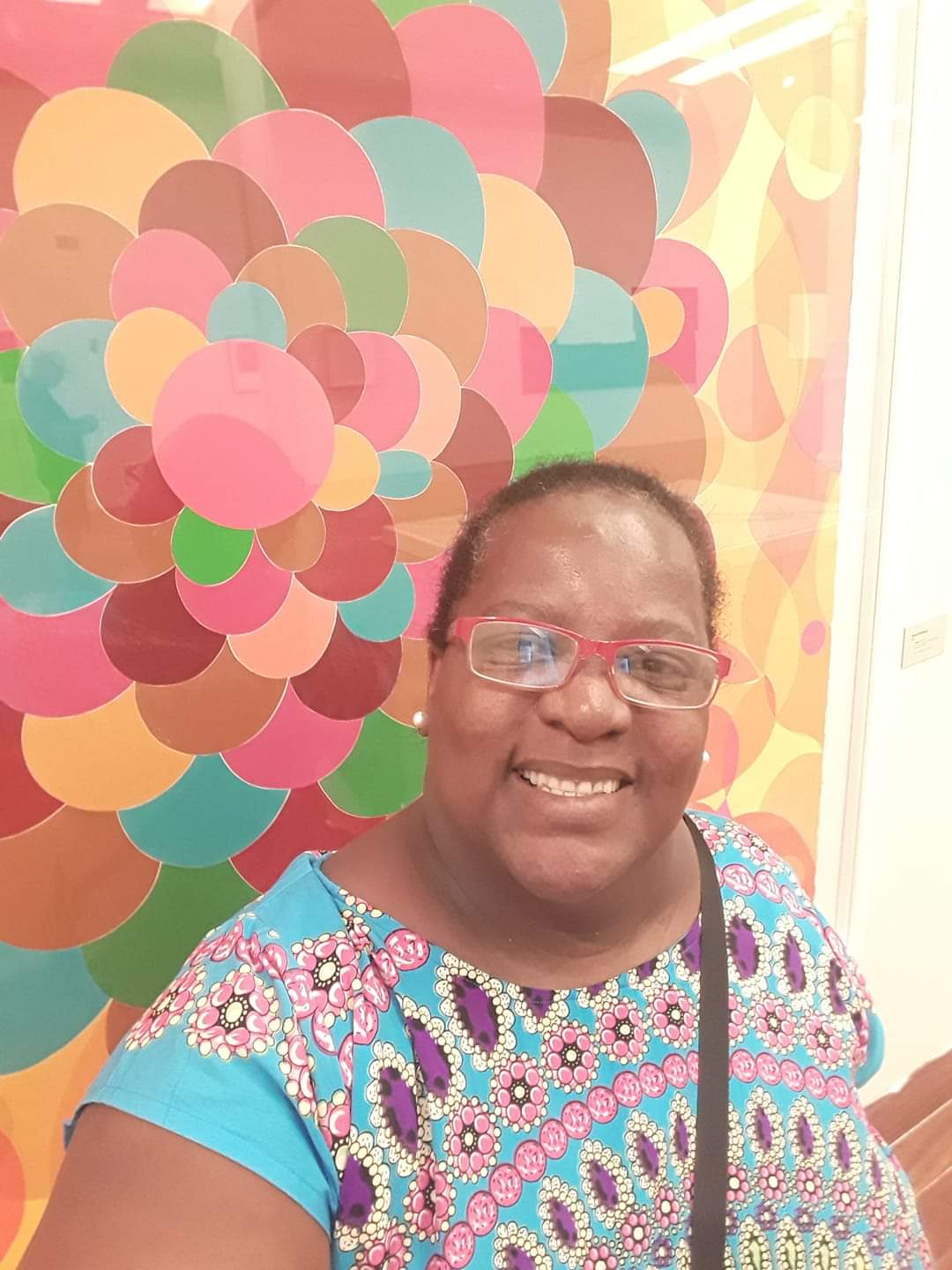 Mulher sorri. Atrás dela, uma parede colorida.