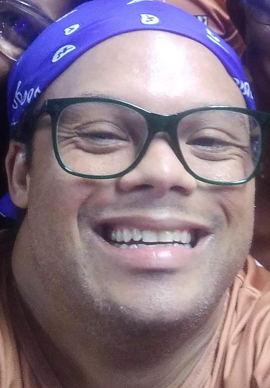 Homem sorri. Ele usa óculos e uma bandana.