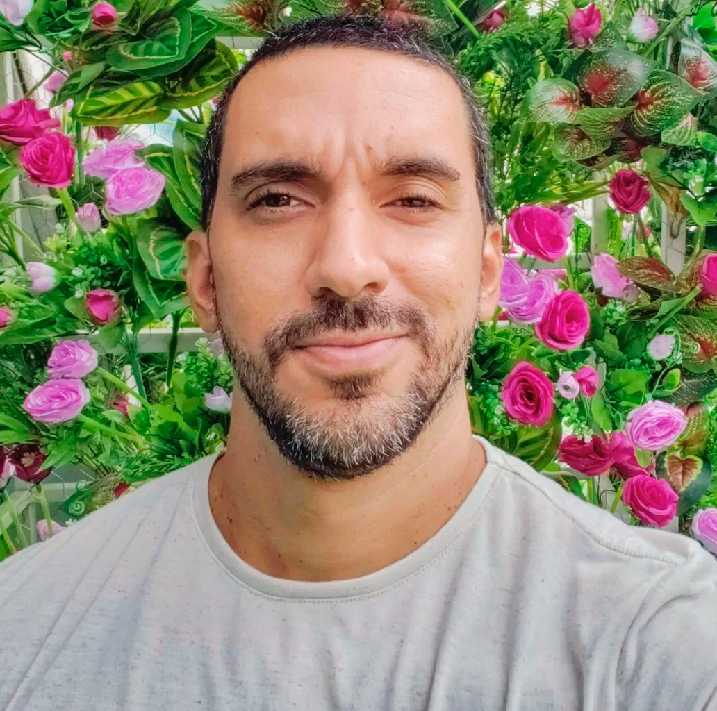 Homem dá leve sorriso. Ao fundo, rosas.