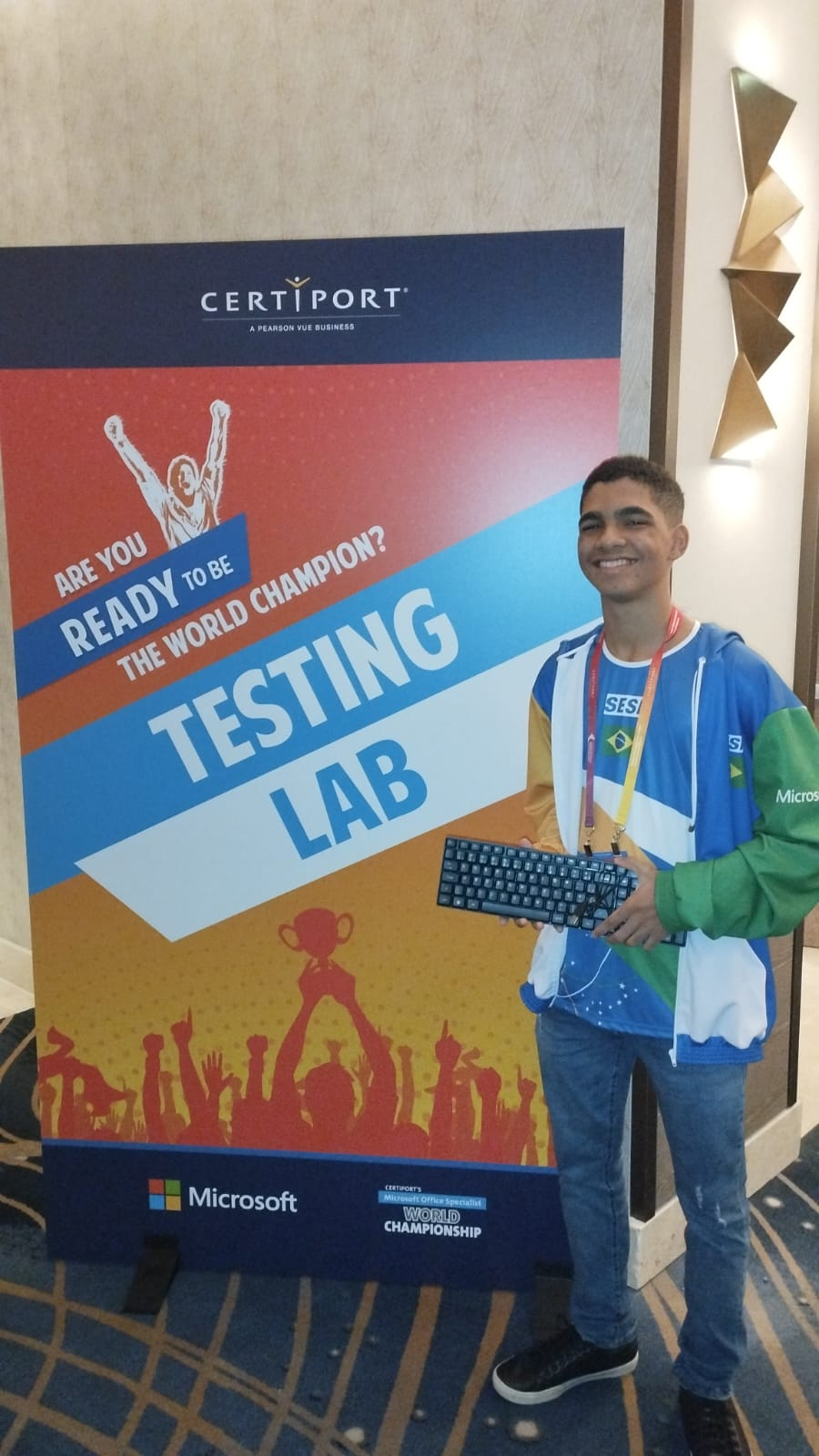 Jovem segura um teclado de computador diante de um cartaz com a escrita "Testing Lab".