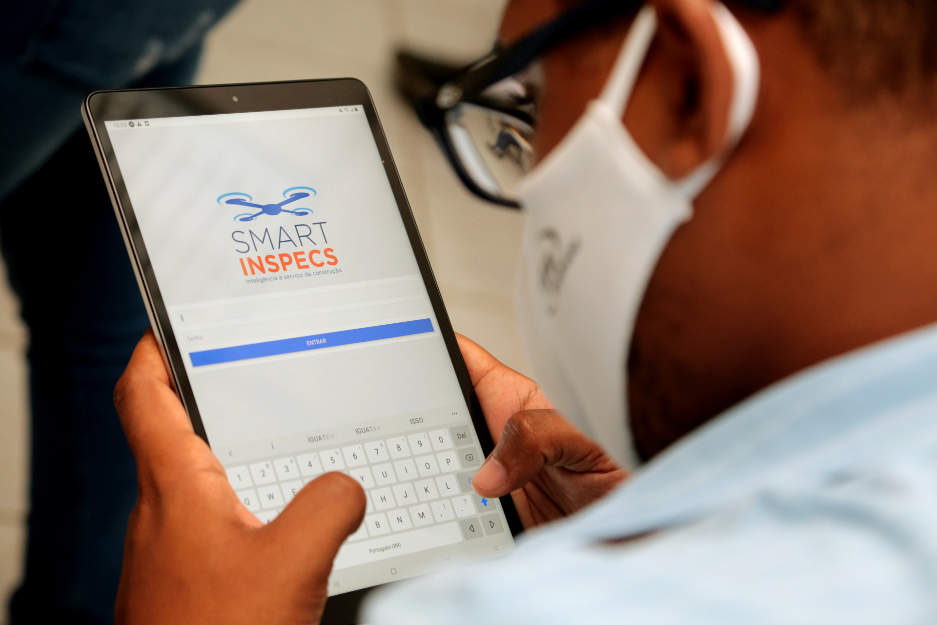Uma pessoa utiliza um tablet. Ela usa máscara.