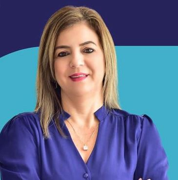 Fundo em azul. Em primeiro plano, uma mulher loira, com valo comprido, sorri levemente.