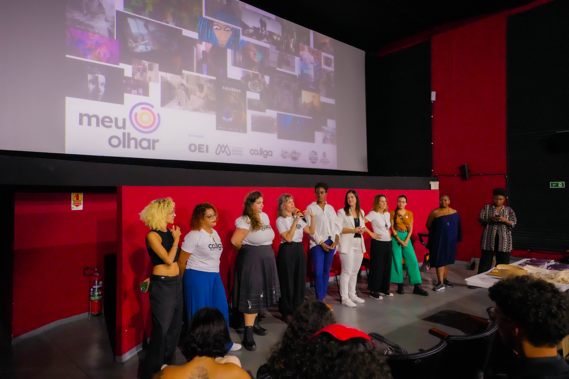 Diversas pessoas de pé sobre o palco de um auditório. Ao fundo, um telão com imagens projetadas.