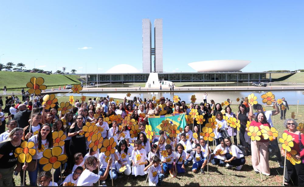 Diversas pessoas estão em um gramado. Atrás delas, o Palácio do Planalto. O dia tinha céu azul, sem nuvens.