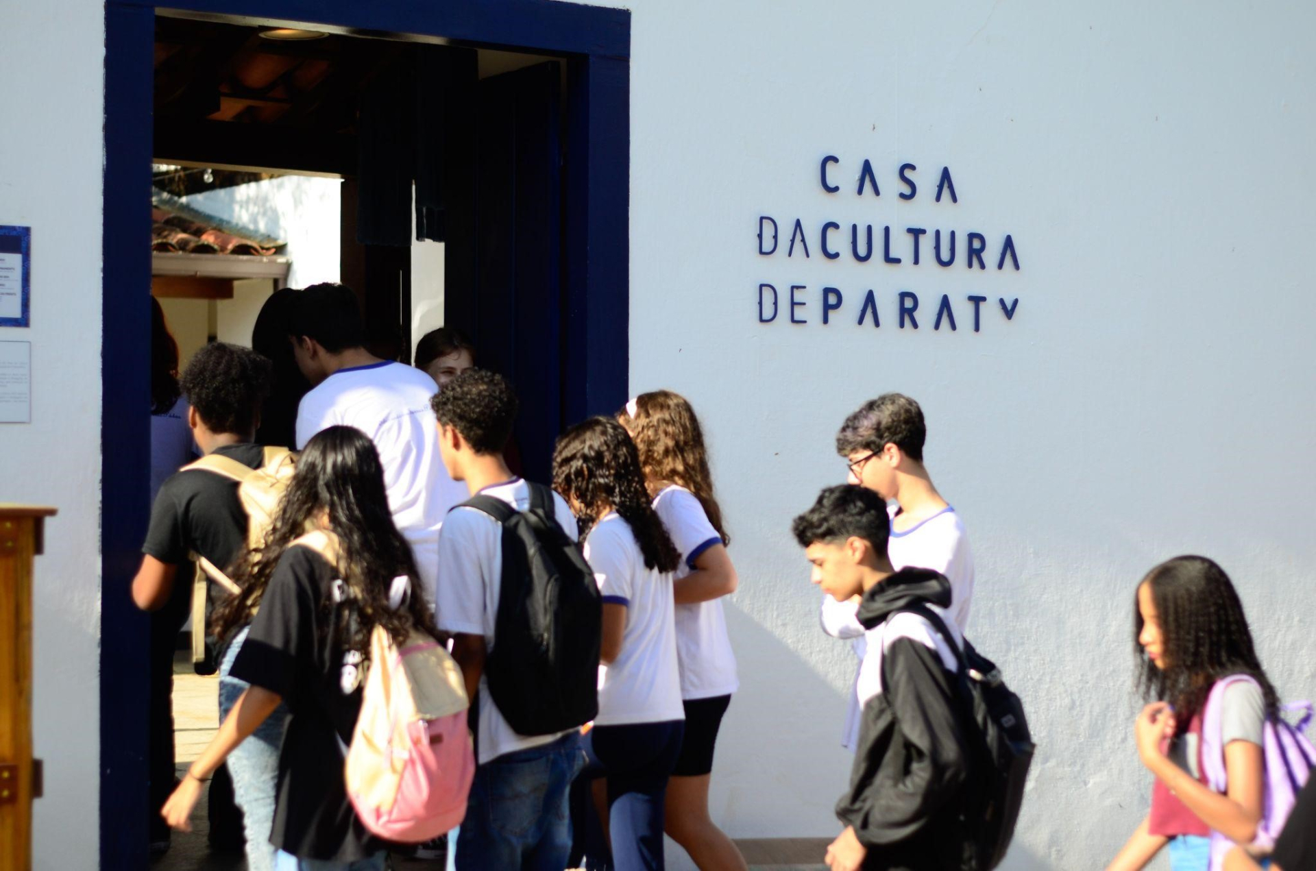 Crianças e adolescentes entrando por uma porta de contorno azul. Na parede branca lê-se "Casa da Cultura de Paraty".