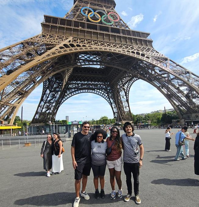 Pessoas de pé. Ao fundo, a Torre Eiffel com o símbolo olímpico.