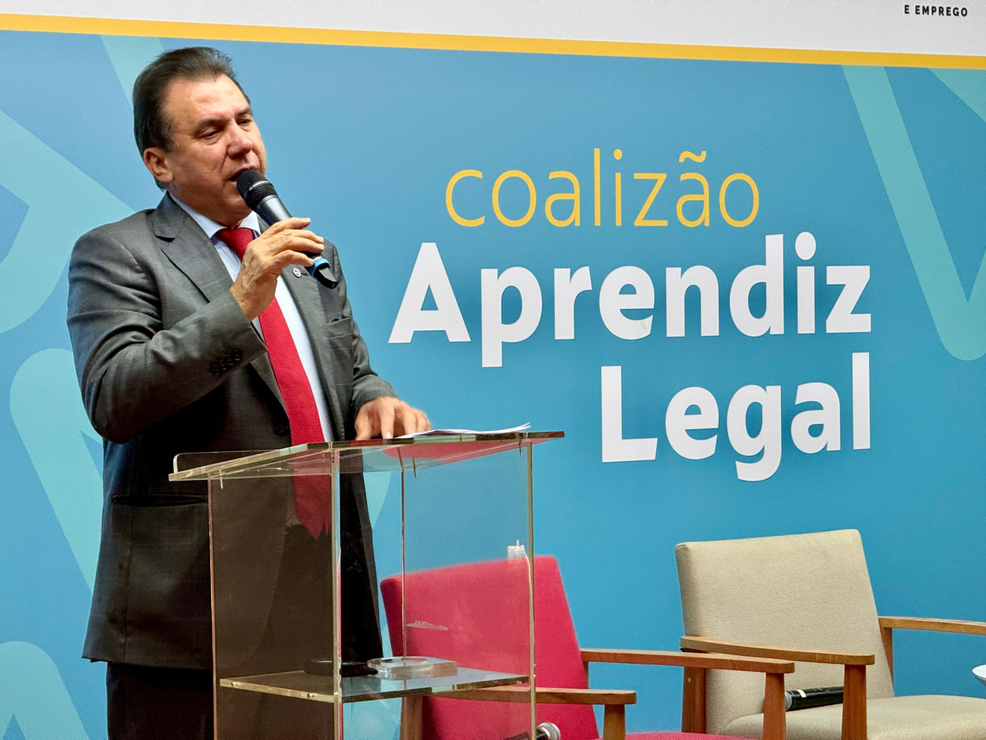 Homem de terno cinza fala ao microfone.