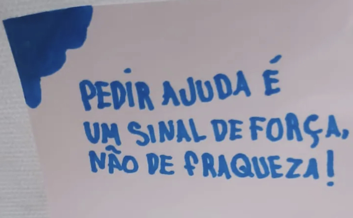 Foto de um cartaz branco com o seguinte texto azul: "Pedir ajuda é um sinal de força, não de fraqueza".