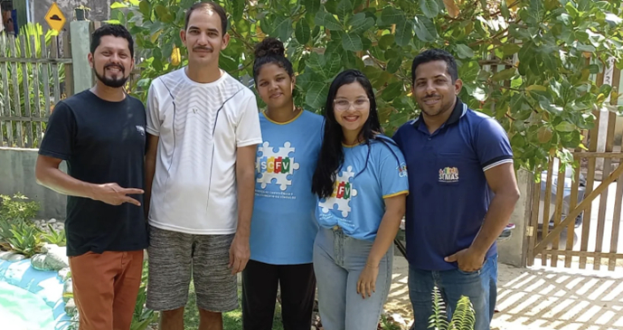 Cinco jovens adultos sorriem, de pé, para quem os fotografa.