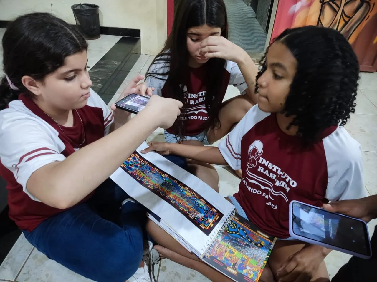 Crianças mexem com folhas de papel e colagens no chão de uma sala de aula.