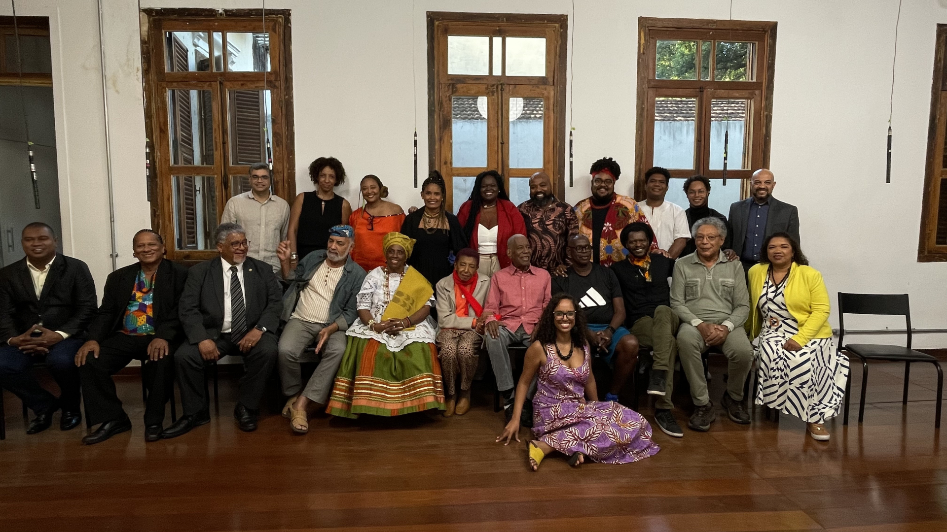 Diversas pessoas sentadas e de pé sorriem para quem as fotografa.