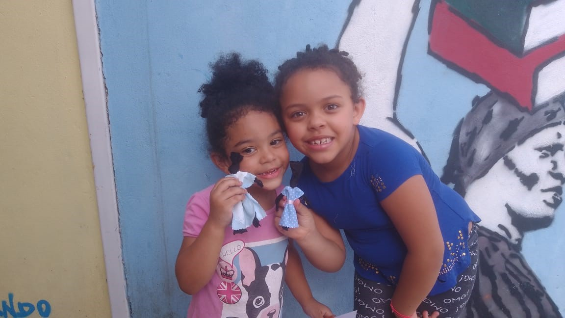 Duas crianças sorrindo e exibindo bonecas de pano para a foto