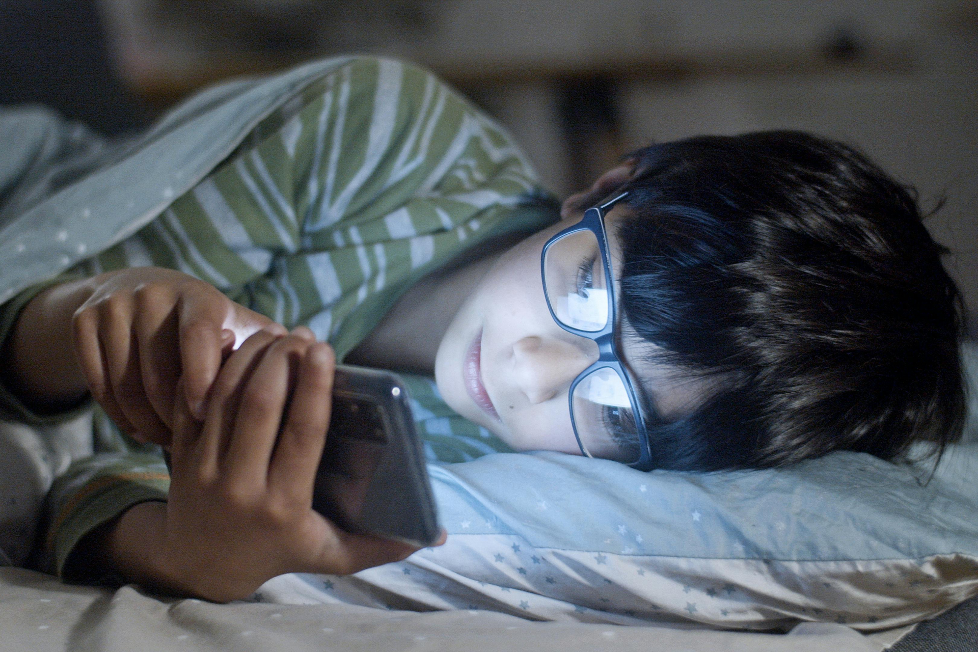 Um menino usando um celular deitado em uma cama