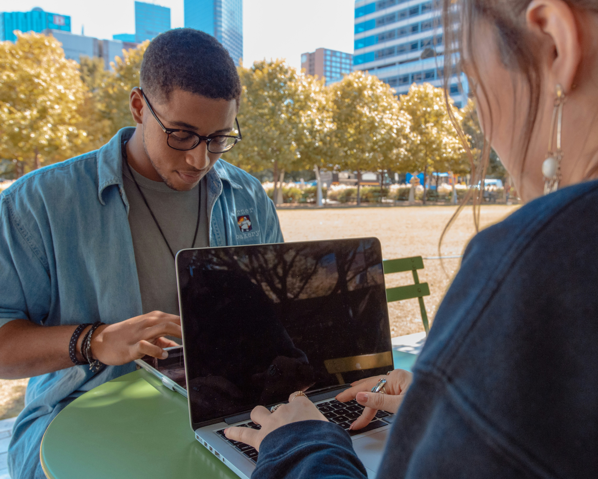 A imagem mostra dois jovens usando notebook em um espaço ao ar livre